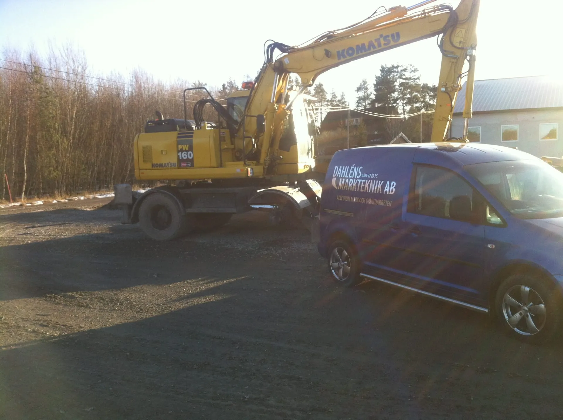 Gul hjulgrävare och blå servicebil med Dahléns Markteknik på sidan, på en grusplan