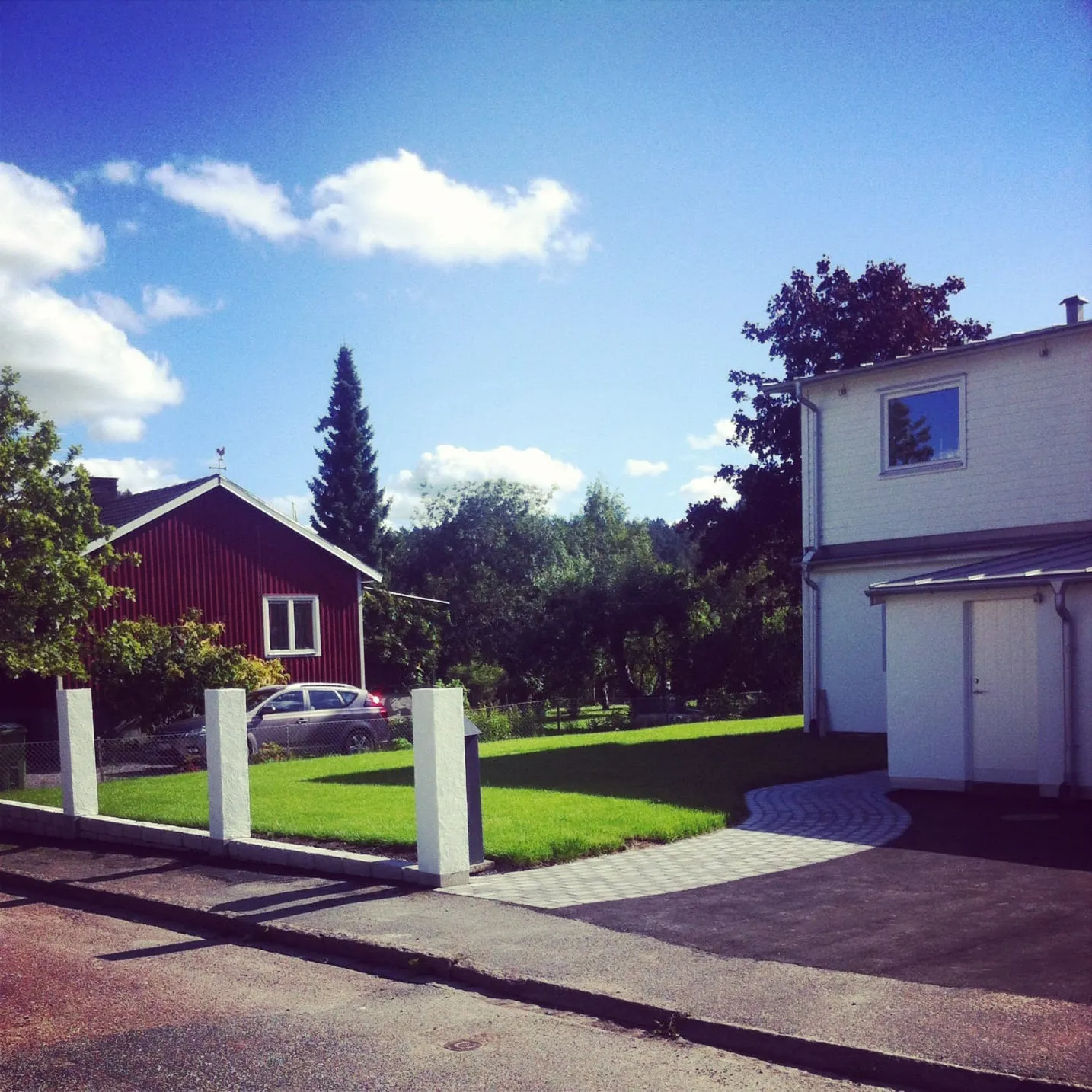 Nyanlagd uppfart med vita stolpar och gräsmatta framför ett vitt hus